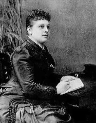 A seated woman in Victorian garb writes in a notebook.
